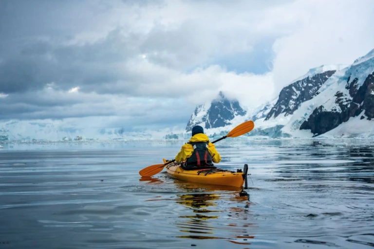 Einzelner Kajakfahrer in Antarktis mit eisbedeckten Bergen an der Küste