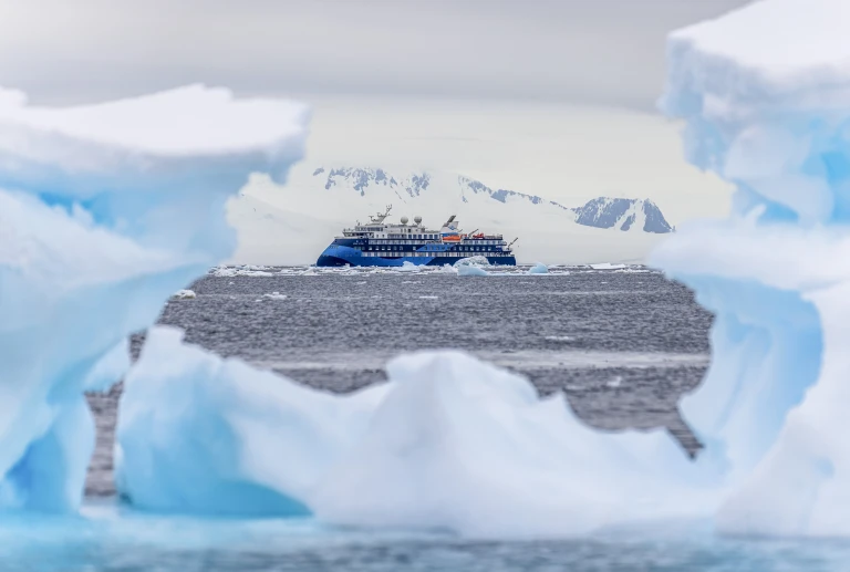 Sie sehen die Ocean Victory von Polar Latitudes Expeditions hinter einem Eisberg in der Antarktis